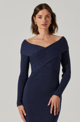 A woman is wearing a fitted, long-sleeved, ribbed knit dress in a dark navy blue color. The dress features a wide, off-the-shoulder neckline that drapes across her shoulders, creating a diagonal seam detail across the bust and waist areas. The fabric has a textured ribbed pattern throughout.